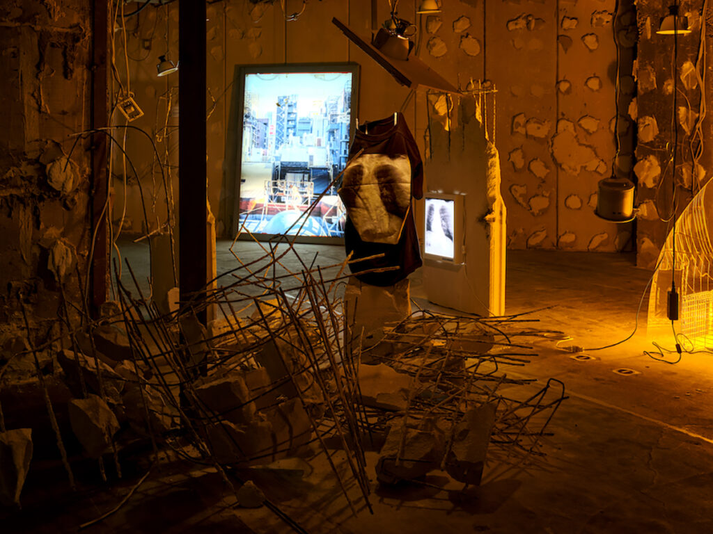 ＜2階＞ 車椅子ダンサー・かんばらけんたはサーチライトを建物の脊椎として解釈し、脊椎が二分されて生まれてきた自身の身体に重ね合わせる。ビルに穴を開け、光が空に直線で伸びるようになるその経緯を「ビルの手術」になぞらえる。ここでは自身のレントゲン写真と、それを自身が着用するためにプリントした私物のTシャツを展示。（撮影：森田兼次）