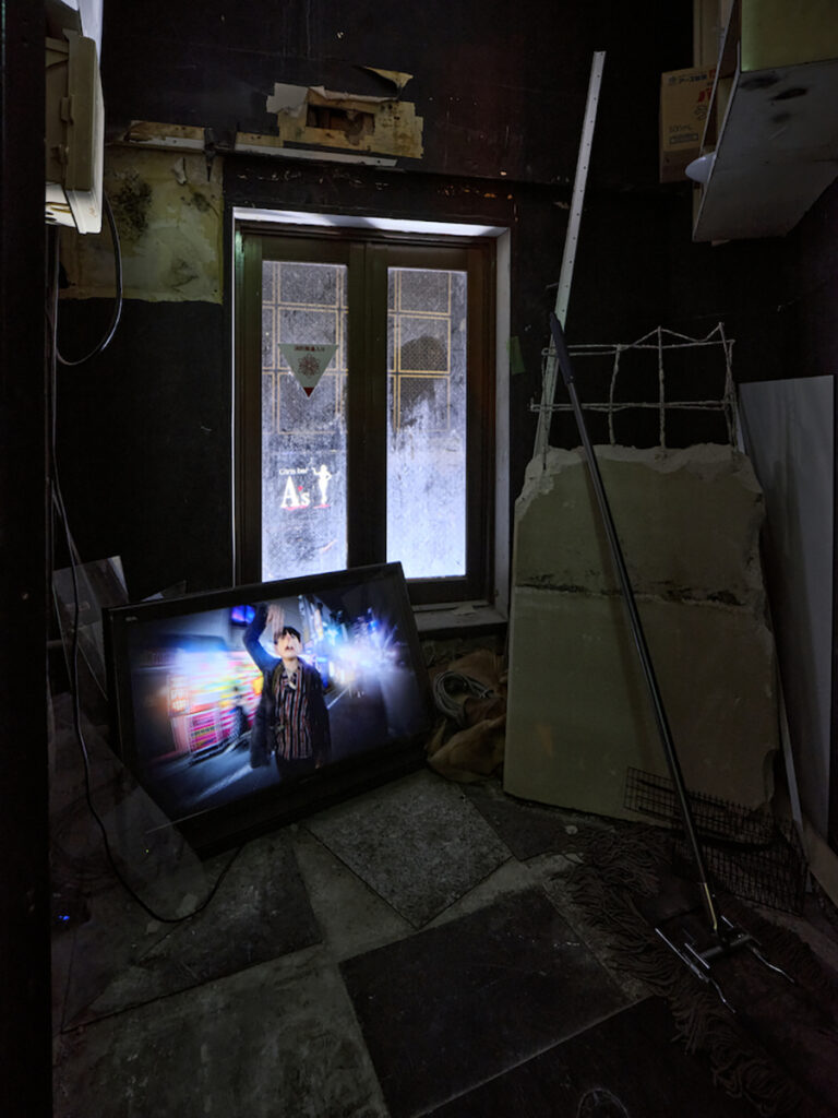 ＜2階＞カラスやネズミの特殊メイクを用いるダンサーの平位蛙は、ネズミとして踊りながら街を徘徊する。360度カメラによる自撮り映像は、常にネズミを中心に捉え編集。そのため周辺 (歌舞伎町の雑沓) は常に歪んでいる。E.には「奈落」での映像を収録。また、隙間を縫うよう館内に分散展示。（特殊メイク: Amazing Jiro）（撮影：森田兼次）