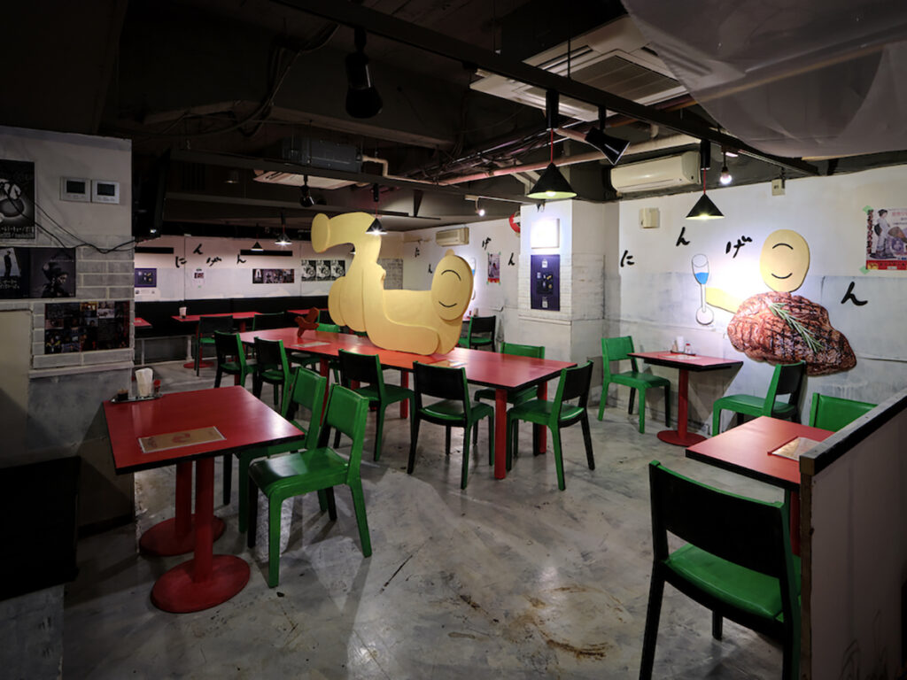 ＜1階＞「にんげんレストラン」2019、2023, インスタレーション, 2018年にChim↑Pomが歌舞伎町ブックセンター跡の廃墟に開店したパフォーマンスベースのレストランプロジェクト「にんげんレストラン」のポップアップ。本家は旧ロボットレストラン前にSmappa!Groupが構える「人間レストラン」。今回はミュージアムカフェ的なポジションとして食に特化し、アメリカの死刑囚が最期にオーダーしたラストミールをはじめ、奈落弁当、地下で養殖されているドクターフィッシュなどのメニューを取り揃える。また、レストランでは歌舞伎超祭のアーカイブ映像を2023年開催分のCMとともに展示。（撮影：森田兼次）