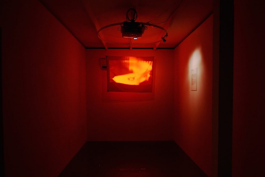 Enduring the Unendurable REAL TIMES, 2015, Even though we received a request from the curator to exhibit REAL TIMES at the Shanghai Biennale in 2012, Chim↑Pom was required to change the exhibiting work at the very last minute. The reason was due to the Senkaku islands dispute, which was intensifying at the time. The problem with the work was the appearance of the Rising Sun flag that one of the members then transformed into a nuclear mark with spray paint, made near the nuclear power plant in Fukushima. This was a rare complaint as this work is often seen to criticize Japan. Massive street demonstrations were happening in Shanghai just before the biennale, and the number of Japanese tourists dropped significantly. Certainly it was a dangerous time. By the way, this work was made into a version to be projected on a red flag in order to neutralize the red circle in the center of the Japanese flag.　2012年の上海ビエンナーレの際、キュレーターから《REAL TIMES》の展示をリクエストされたが、直前になって展示作品の変更を要請される。当時激化していた尖閣諸島問題が原因だった。メンバーが原発の近くで旗に改変していくマークをスプレーで描くのだが、いちど日の丸になっているのが問題とのこと。日本Disと受け取られがちな本作にしてはめずらしいタイプのクレームだった。ビエンナーレ直前にも上海で大規模な反日デモが起き、日本人観光客も激減していたときだった。つまり、確かに危ない時期ではあった。ちなみに本作品は、赤い旗にプロジェクションをして、日の丸の赤を相殺するバージョンである。